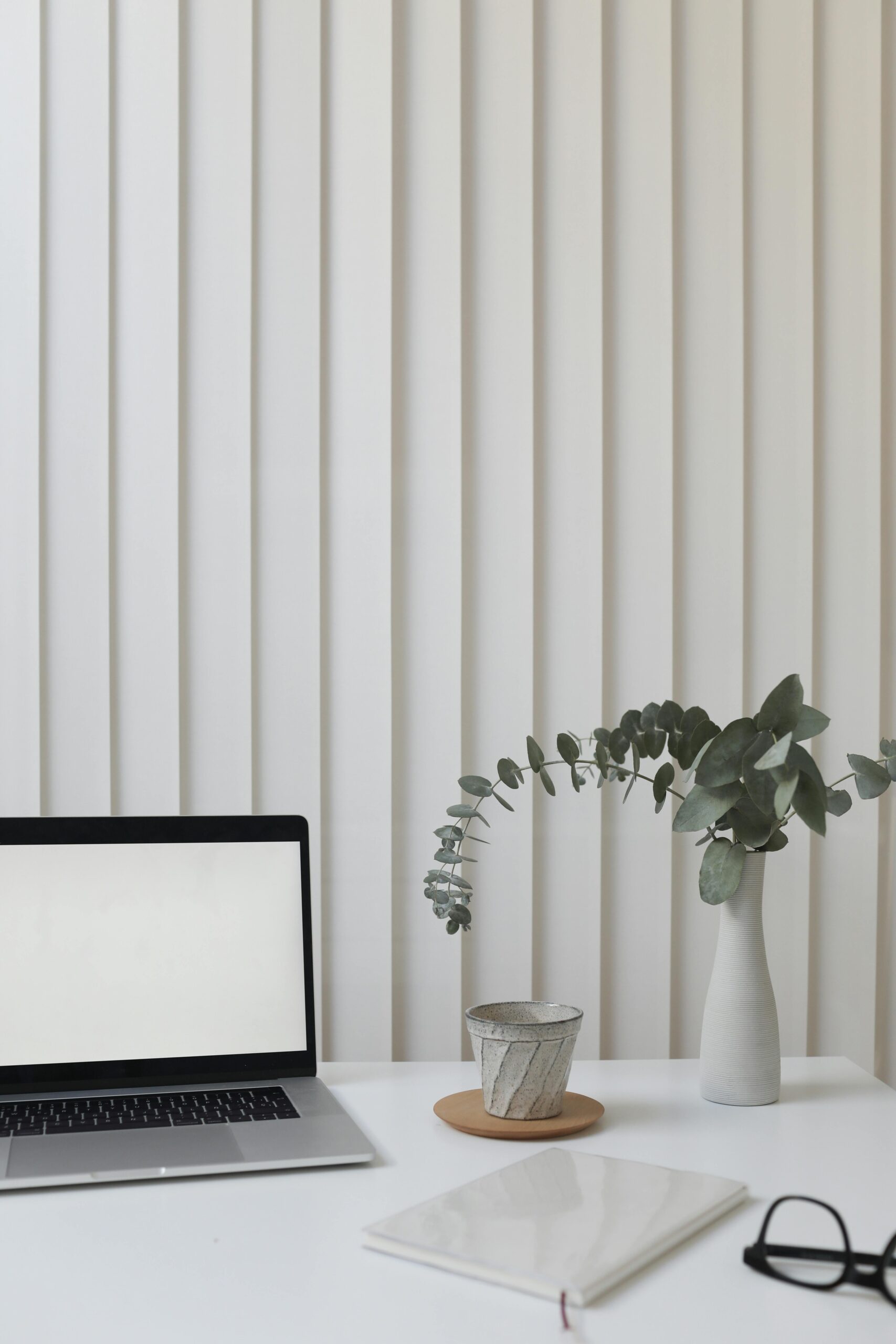 A clean and modern workspace featuring a laptop, vase with greenery, and notepad.